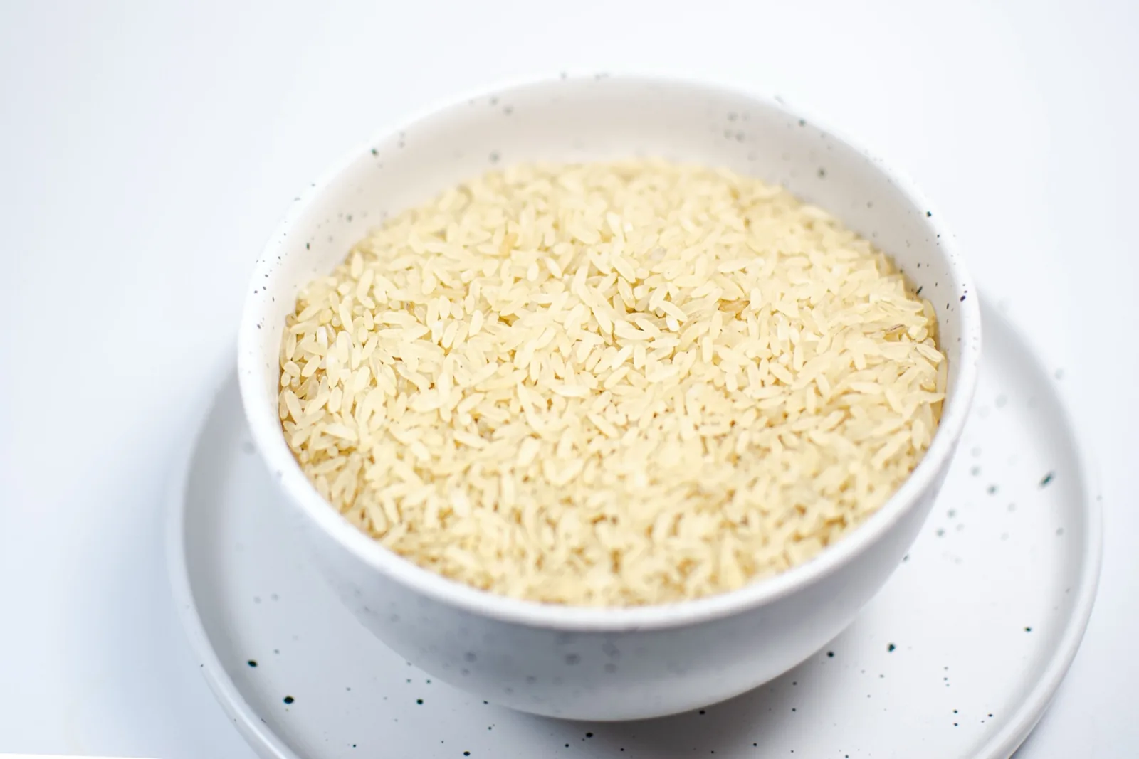 Editorial photograph of loose raw rice in a plain bowl